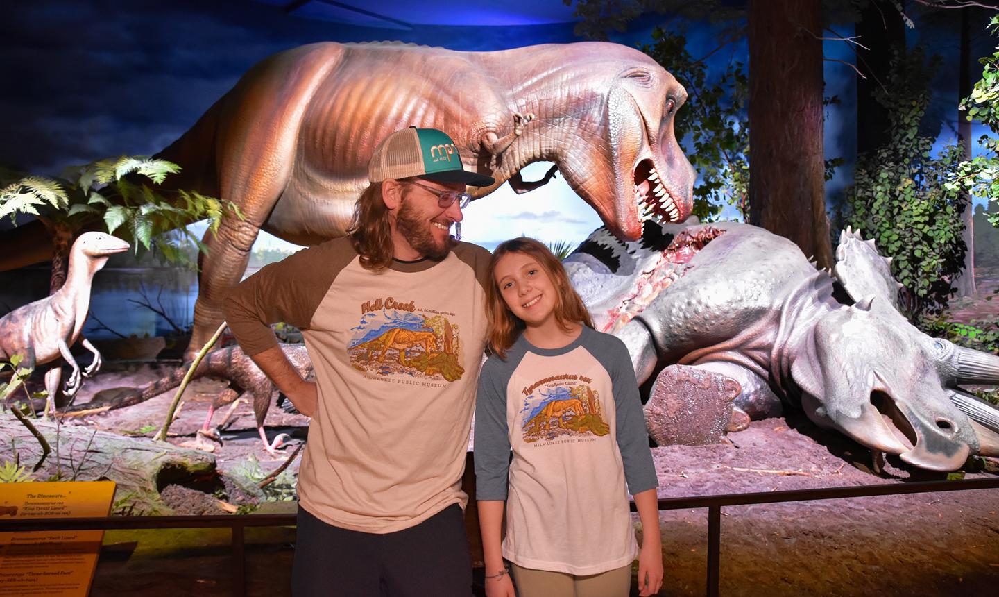 Father and Daughter in MPM gear standing in front of Hell Creek dinosaur exhibit